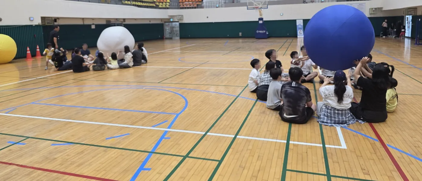 체육관에서 대형 공을 둘러싸고 앉은 아이들