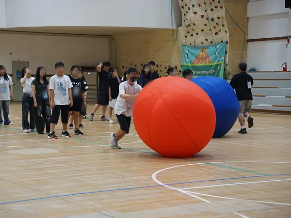체육관에서 학생들이 대형 빨간 공과 파란 공을 굴리는 명랑운동회