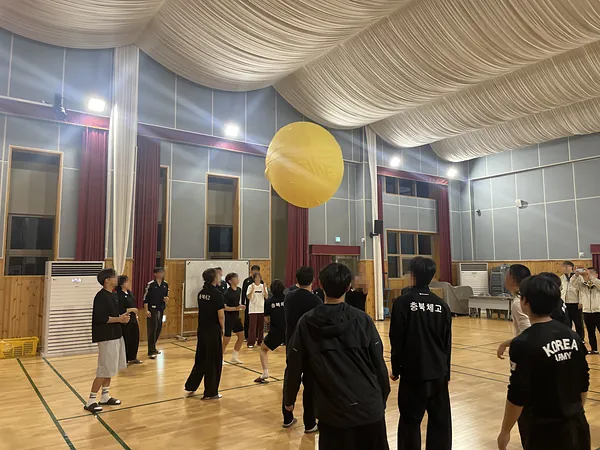 학생들이 노란 대형 공을 체육관 천장 가까이 띄워 올리는 모습