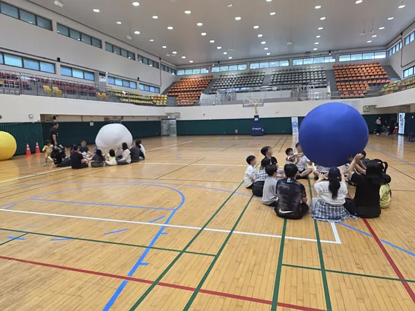 체육관에서 아이들이 대형 공을 함께 굴리는 명랑운동회